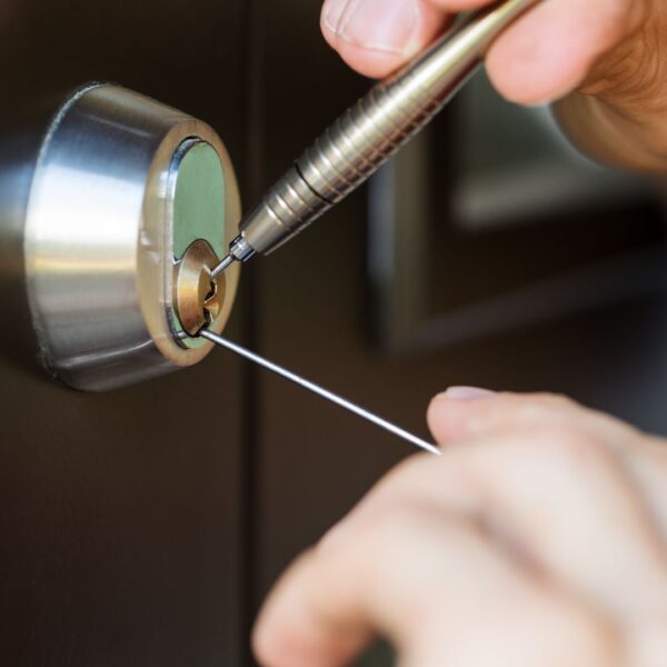 A locksmith's hands using a pick tool to work on the inside of a deadbolt lock.